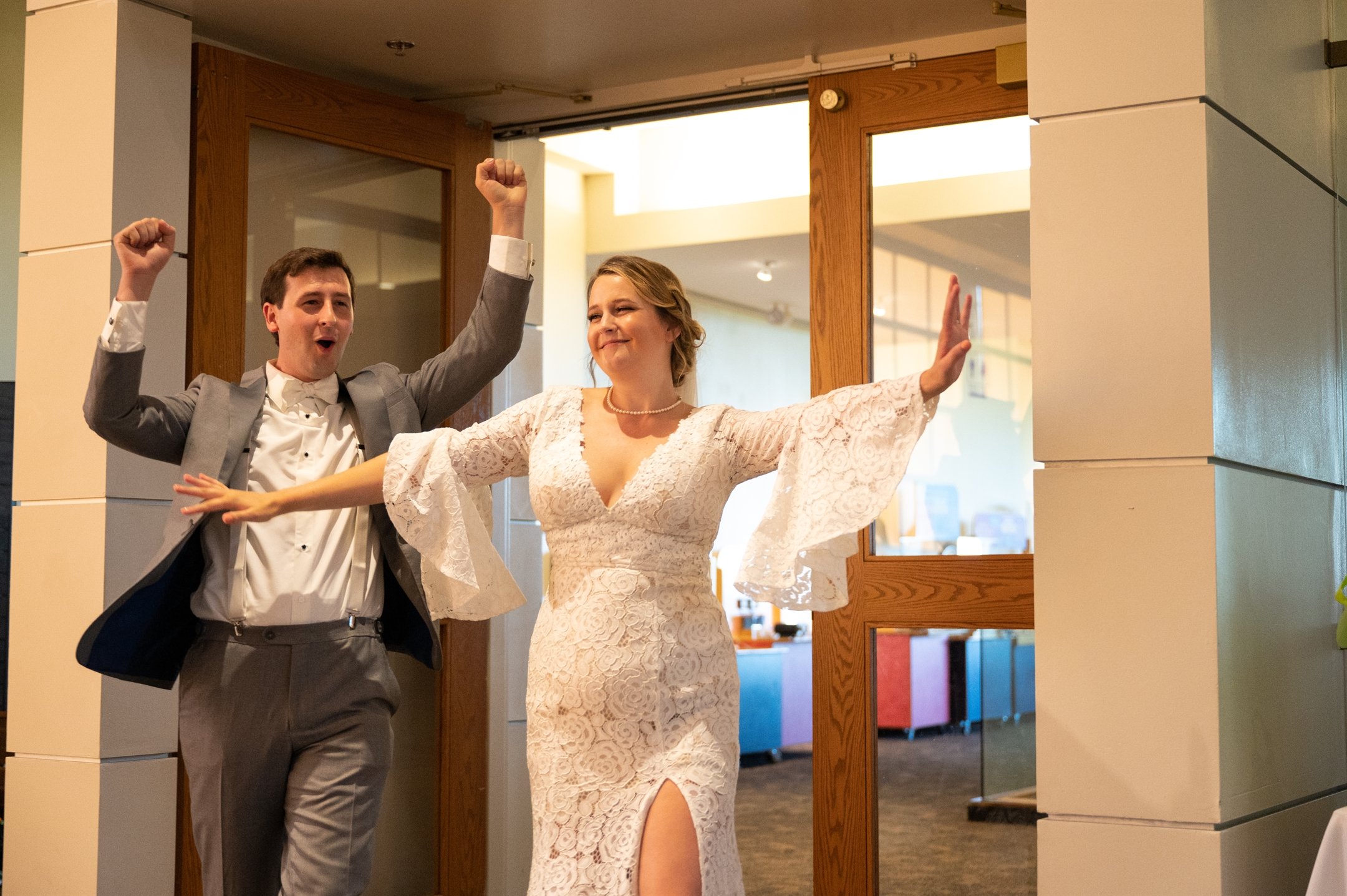 Bride and groom celebrating entrance at wedding reception, woman in lace dress and man in gray suit.