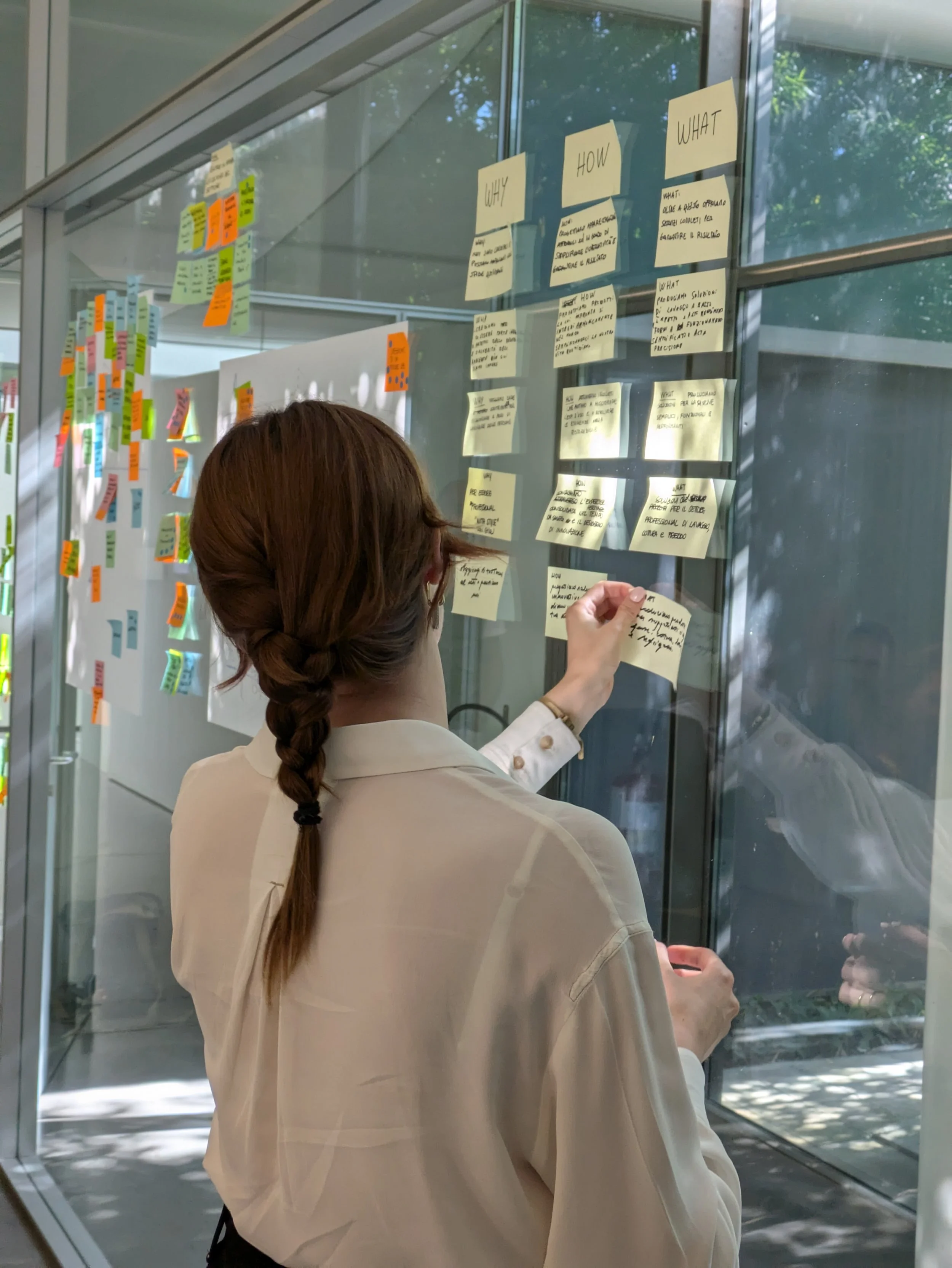 Donna con treccia castana che scrive su un post-it in uno studio moderno.