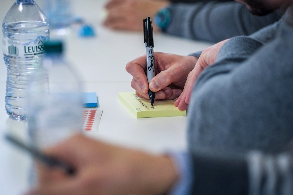 Persona che scrive appunti su un blocco di post-it durante un workshop.