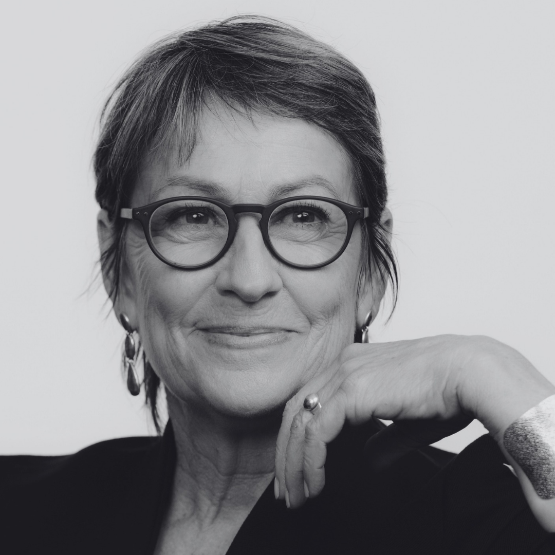 A woman with short layered hair wearing a black turtleneck and earrings, smiling slightly, in a black and white portrait against a light background.