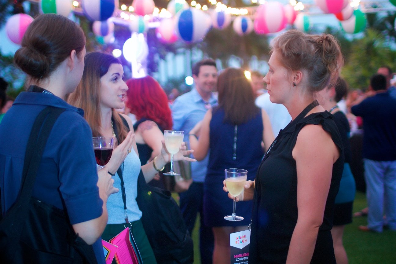 Group of people socializing at an outdoor party with colorful hanging paper lanterns, some holding drinks like wine and cocktails.