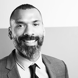 Close-up of a young woman with brown hair and brown eyes smiling, showing her teeth, with a blurred background.