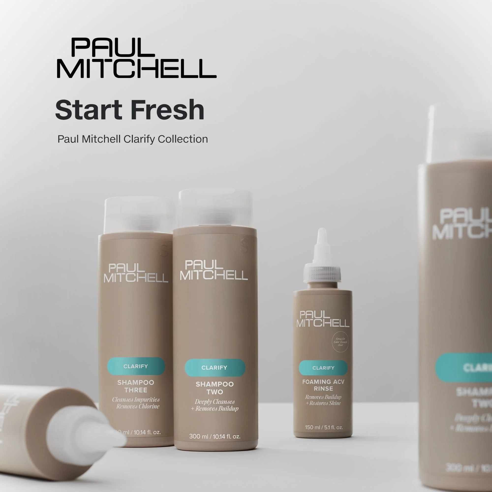 Four beige bottles of Paul Mitchell Clarify hair products with white caps on a white surface against a light gray background. One bottle is lying down, and the others are upright, with labels indicating shampoo and rinse.
