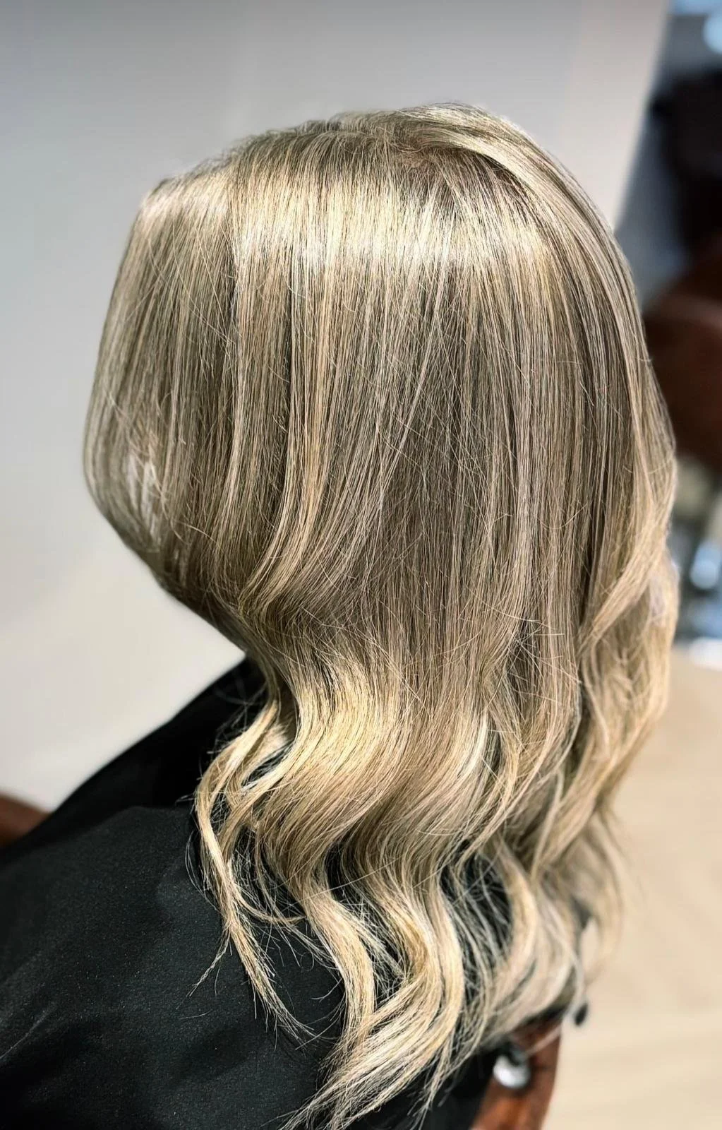 Close-up of wavy blonde hair with highlights on a person's head, viewed from the back.