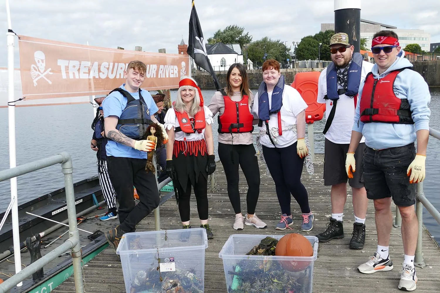 A group of people in life vests are proudly showing off their 'catch' of litter from their plastic fishing trip.