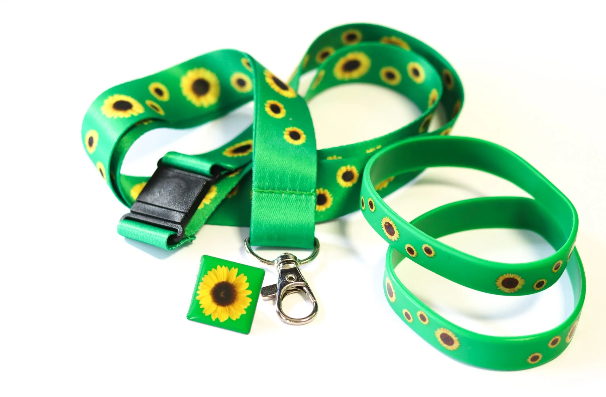 A green lanyard with sunflowers in it, used to highlight the wearer has a hidden disability. Next to it are two sunflower wristbands