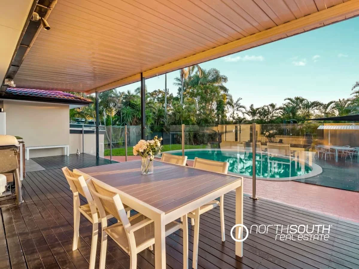 Timber deck with outdoor table, chairs and barbeque overlooking the backyard, pool and palm trees at sunset at 7 Bligh Street, Rochedale South QLD 4123