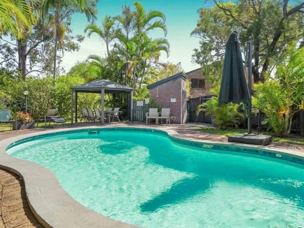 Outdoor pool with shaded seating and tropical landscaping in Townhouse complex in Labrador QLD.