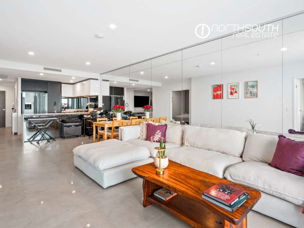 Open-plan living and dining area with mirrored wall and balcony views at 51109 5 Harbourside Ct, Waterpoint Residences, Biggera Waters QLD.