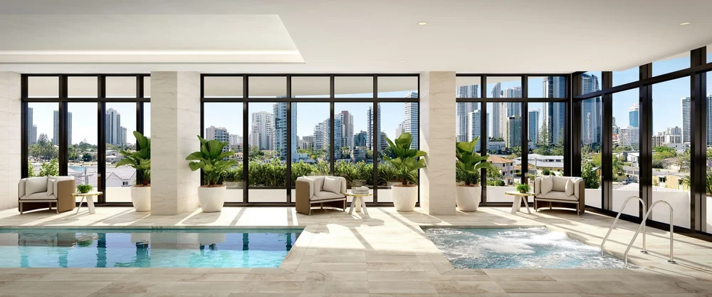 Indoor swimming pool area with large windows showing city skyline, white lounge chairs, potted green plants, and a hot tub.