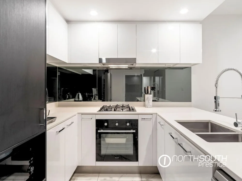 Contemporary white kitchen with gas cooktop, mirrored splashback, and tiled floors at Waterpoint Residences, Biggera Waters QLD.