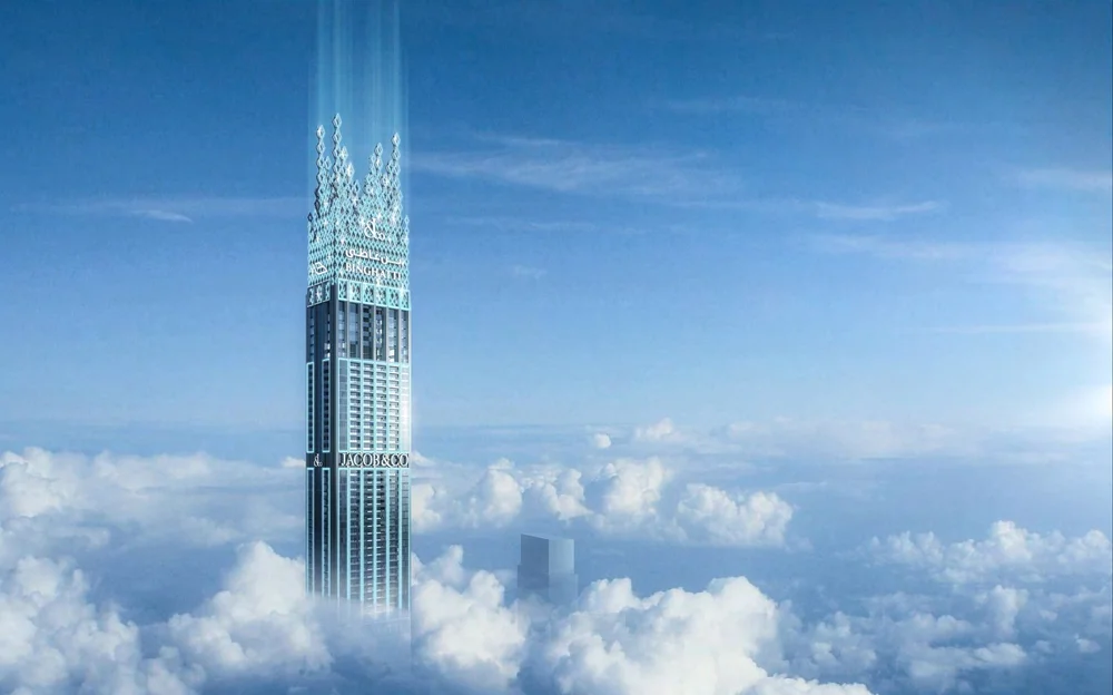 A tall skyscraper called Jacob & Co. Binghatti rises above clouds in the sky with a blue and white exterior and a unique pointed top design.