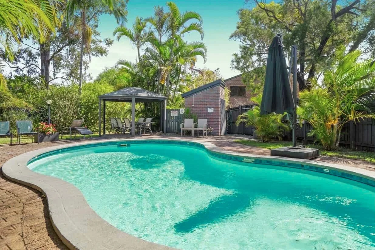 Outdoor pool with shaded seating and tropical landscaping in apartment complex in Labrador QLD.