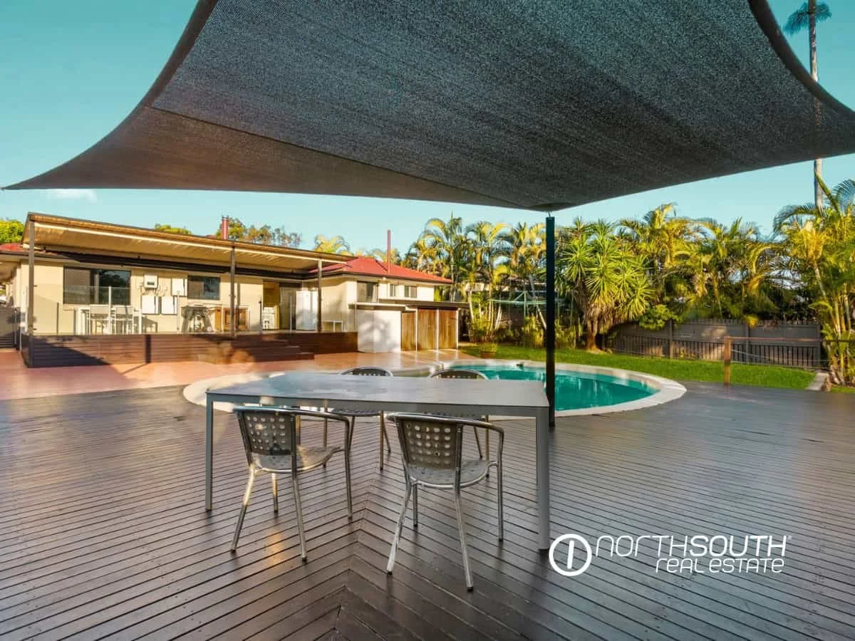 Timber deck with outdoor table and chairs  overlooking the back of the house, pool and palm trees at 7 Bligh Street, Rochedale South QLD 4123