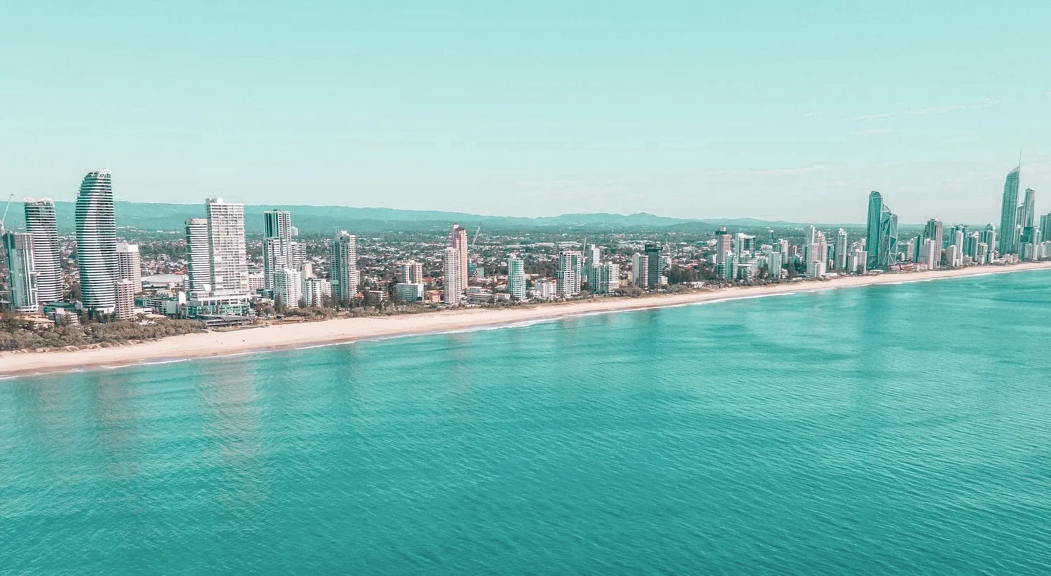 Aerial view of a city skyline with high-rise buildings along a beach and turquoise ocean waters