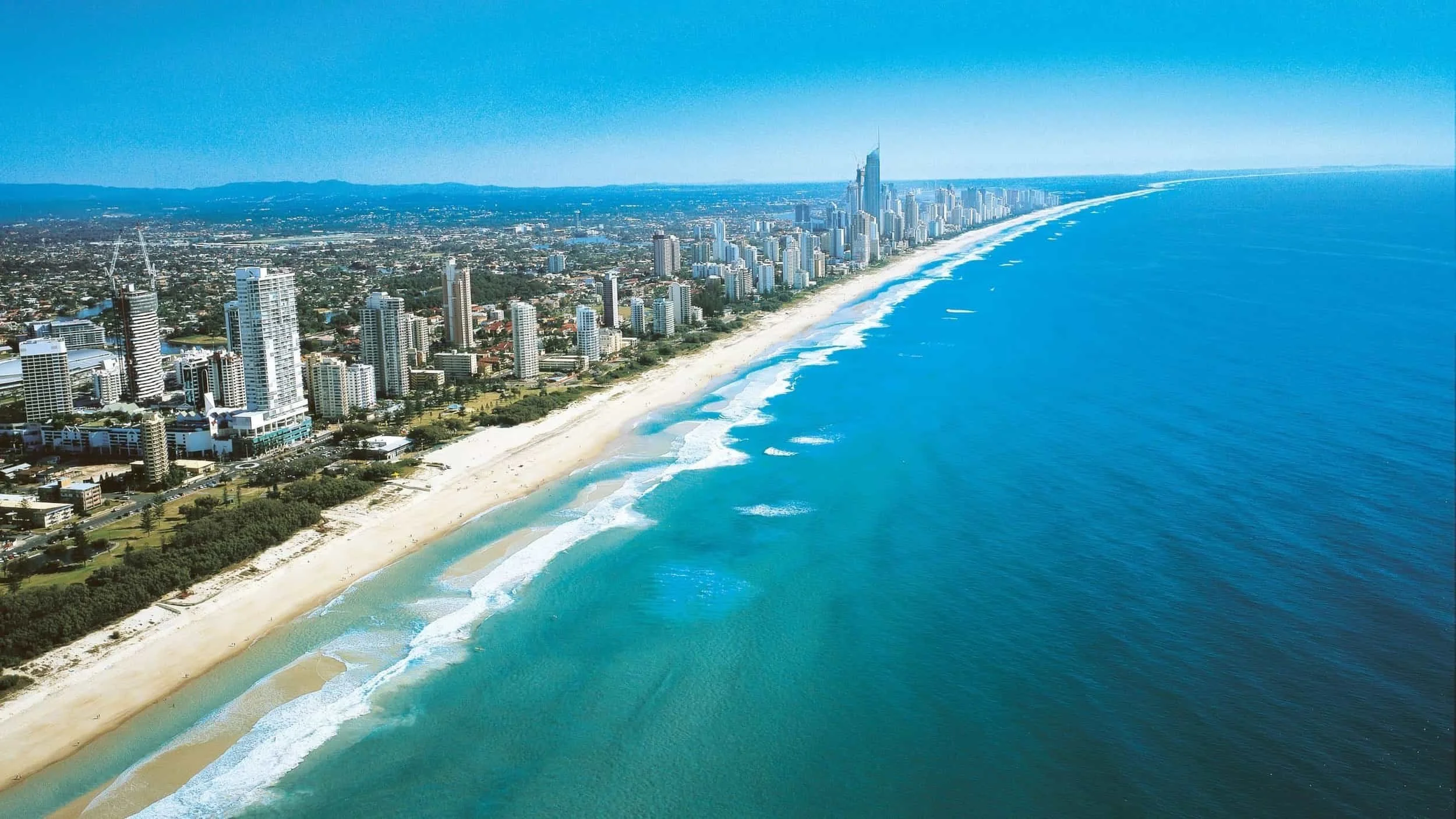 Aerial view of a city skyline along a beach with high-rise buildings and clear blue ocean waves.