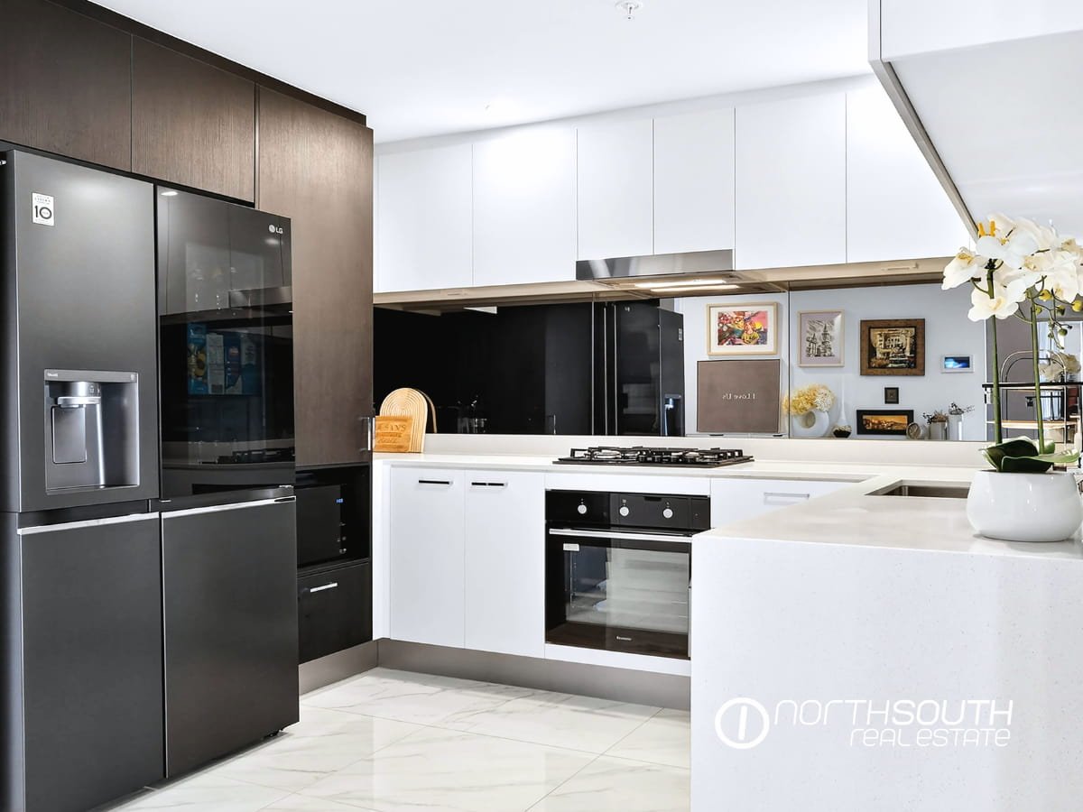 Modern white kitchen with gas cooktop, mirrored splashback and tiled floors at 4705 Waterpoint Residences, Biggera Waters QLD.