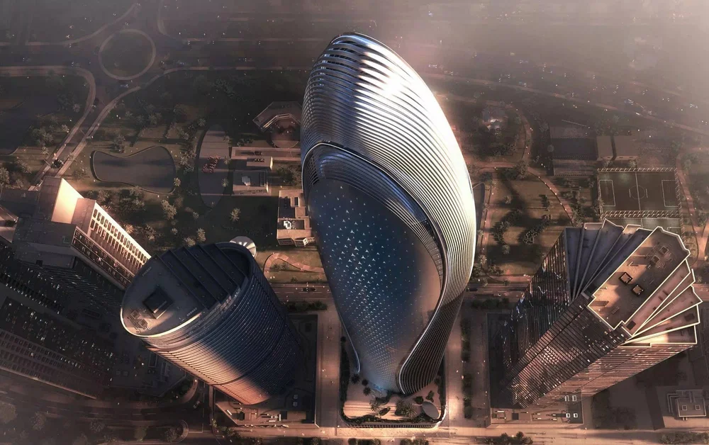 An aerial view of futuristic tall skyscrapers with curved, sleek designs in a city with roads, parks, and sports courts.
