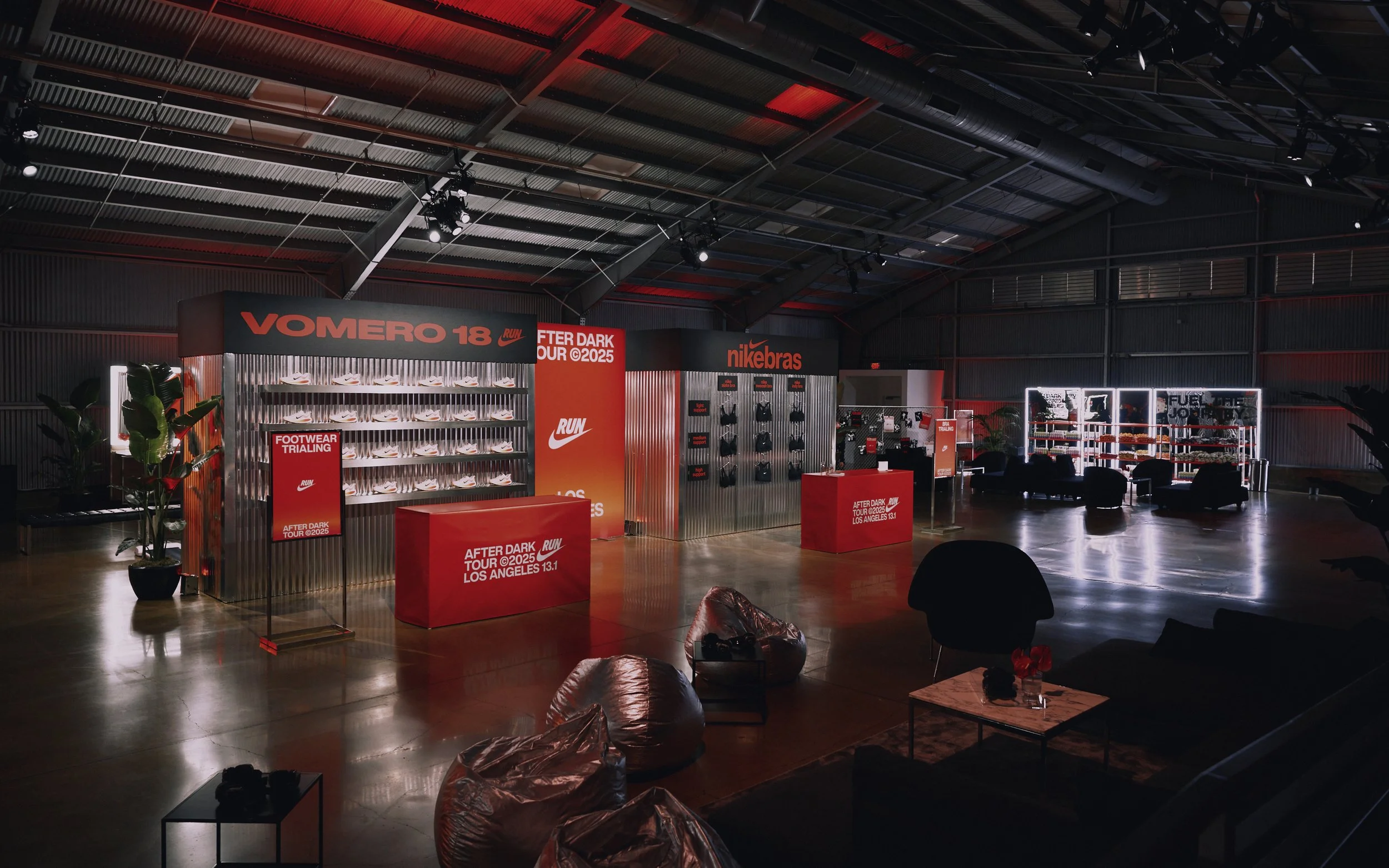 An indoor Nike event space with red and black decor, displaying Nike sneakers, footwear trial signs, and seating areas for visitors.