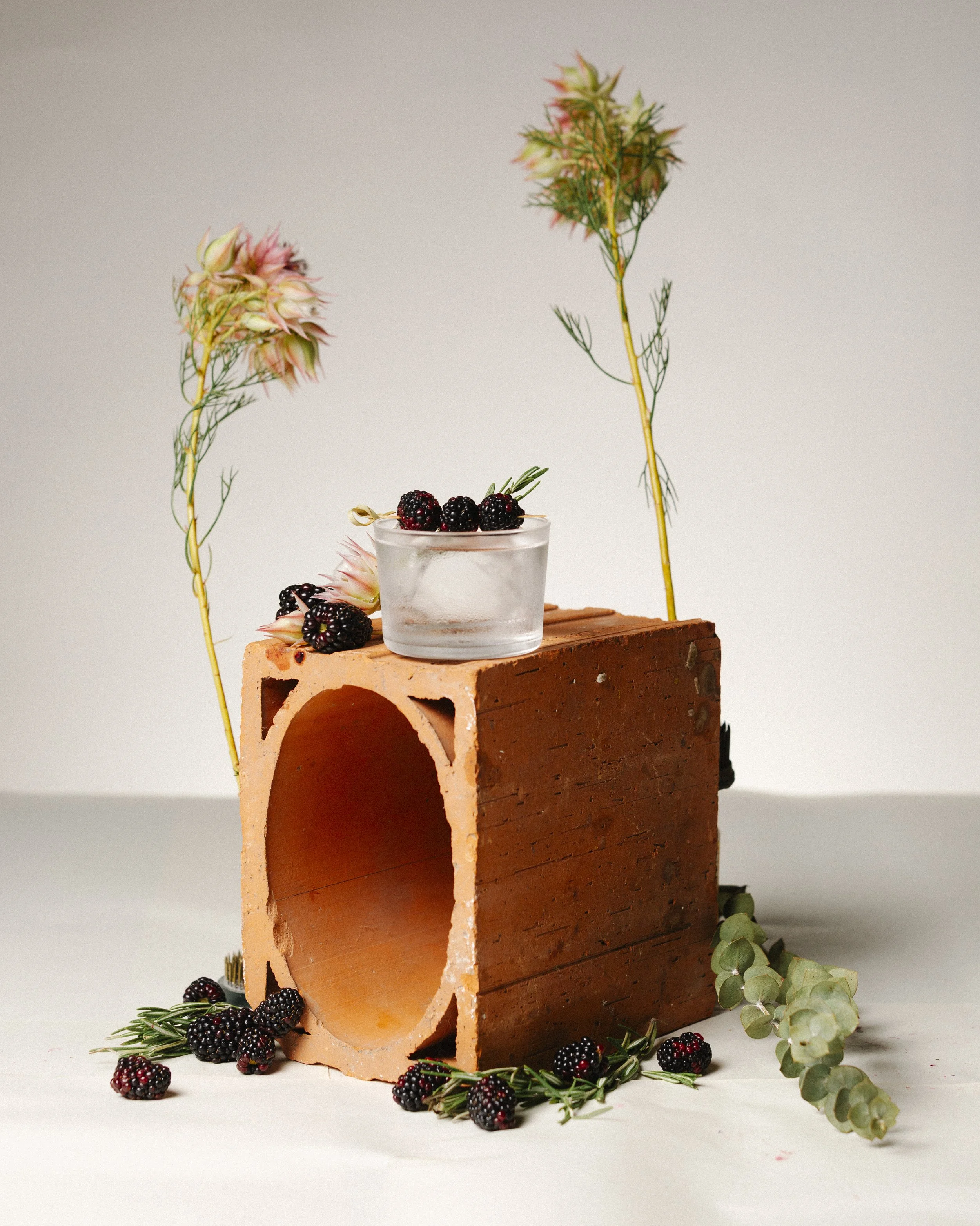 A decorative display with a terracotta brick, berries, flowers, and greenery, set against a neutral background.