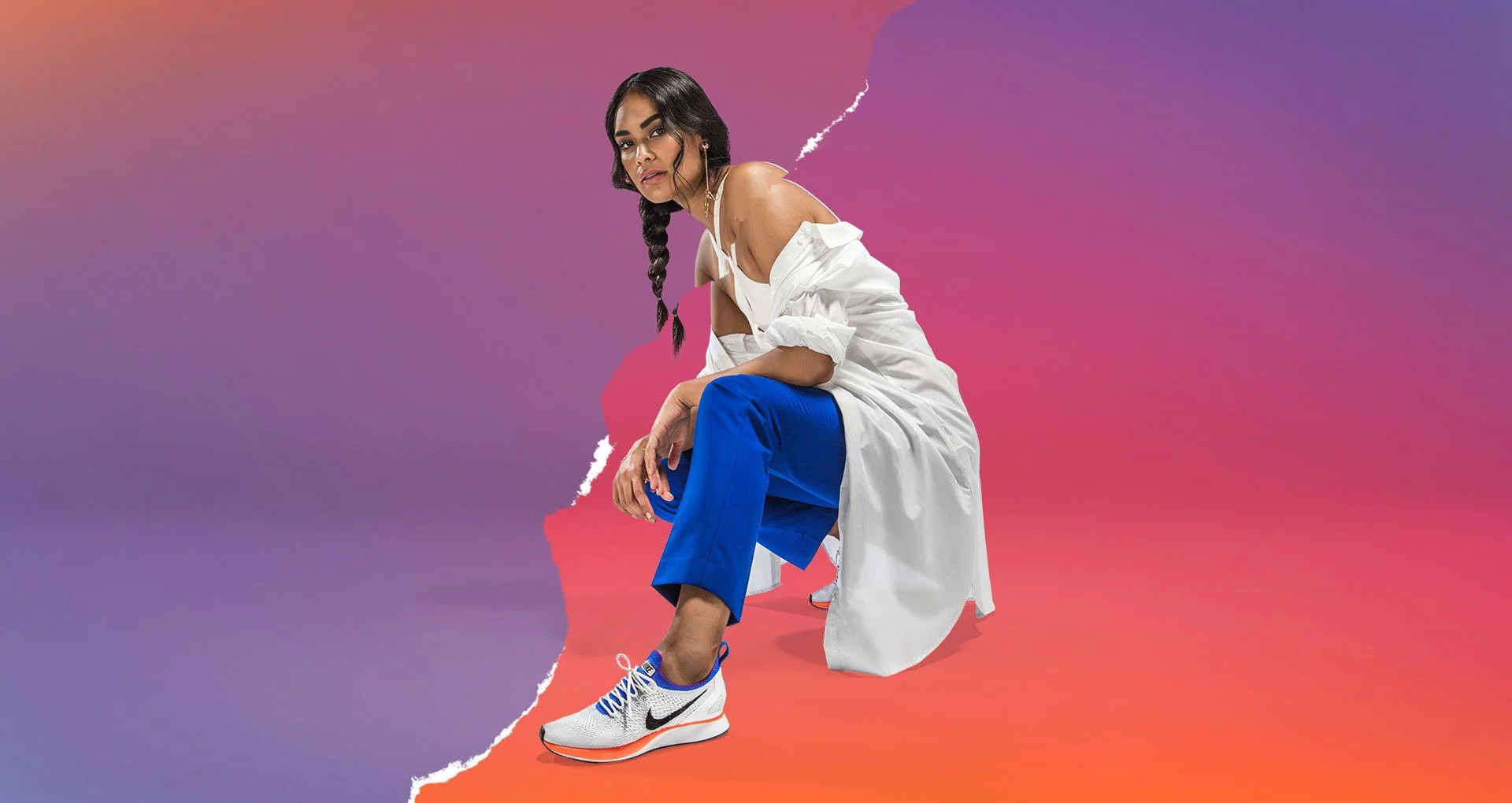 Young woman with braided hair crouching in front of a colorful, abstract gradient background with torn paper edges, wearing a white off-shoulder jacket, blue pants, and white Nike sneakers.