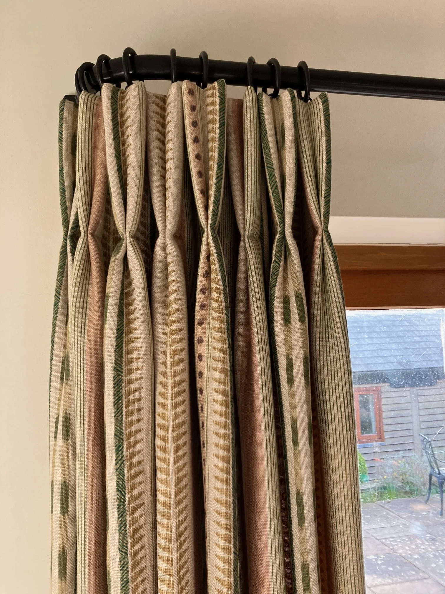 Interlined curtain with a striped abstract pattern, double pinch pleat header hanging on french pole in front of a window.
