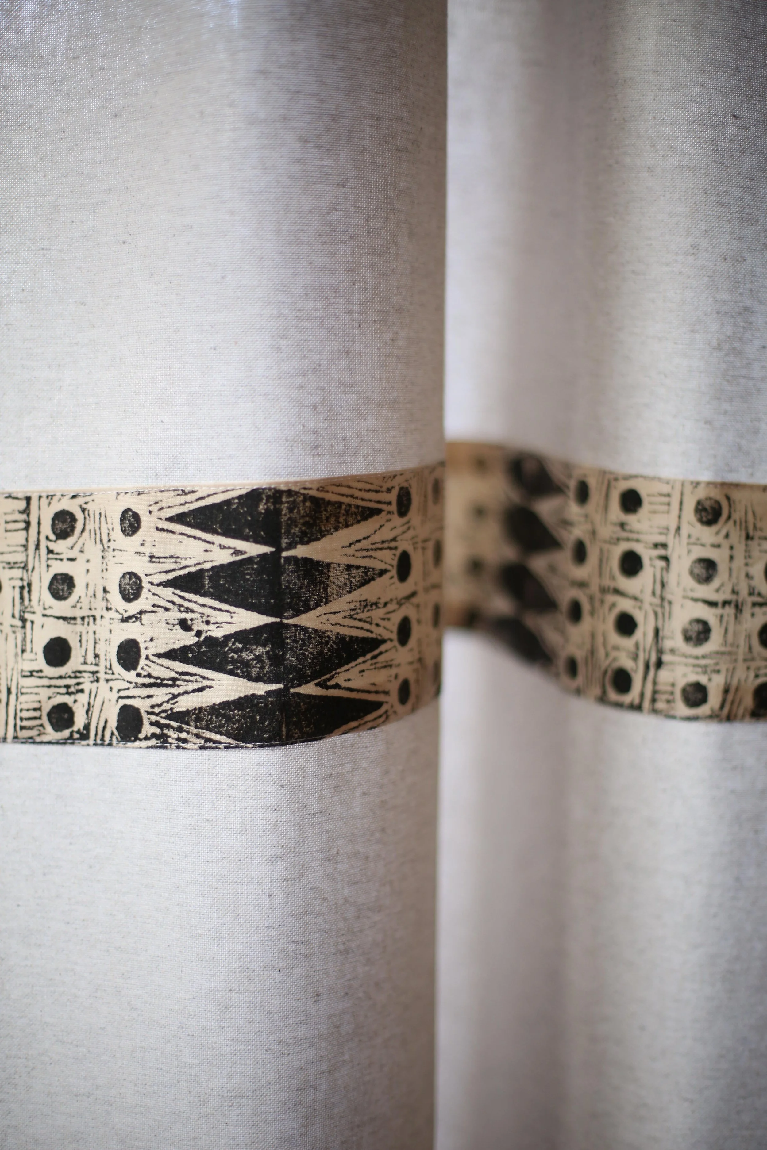 Close-up of a curtain with a border featuring a black geometric pattern and a textured beige background.
