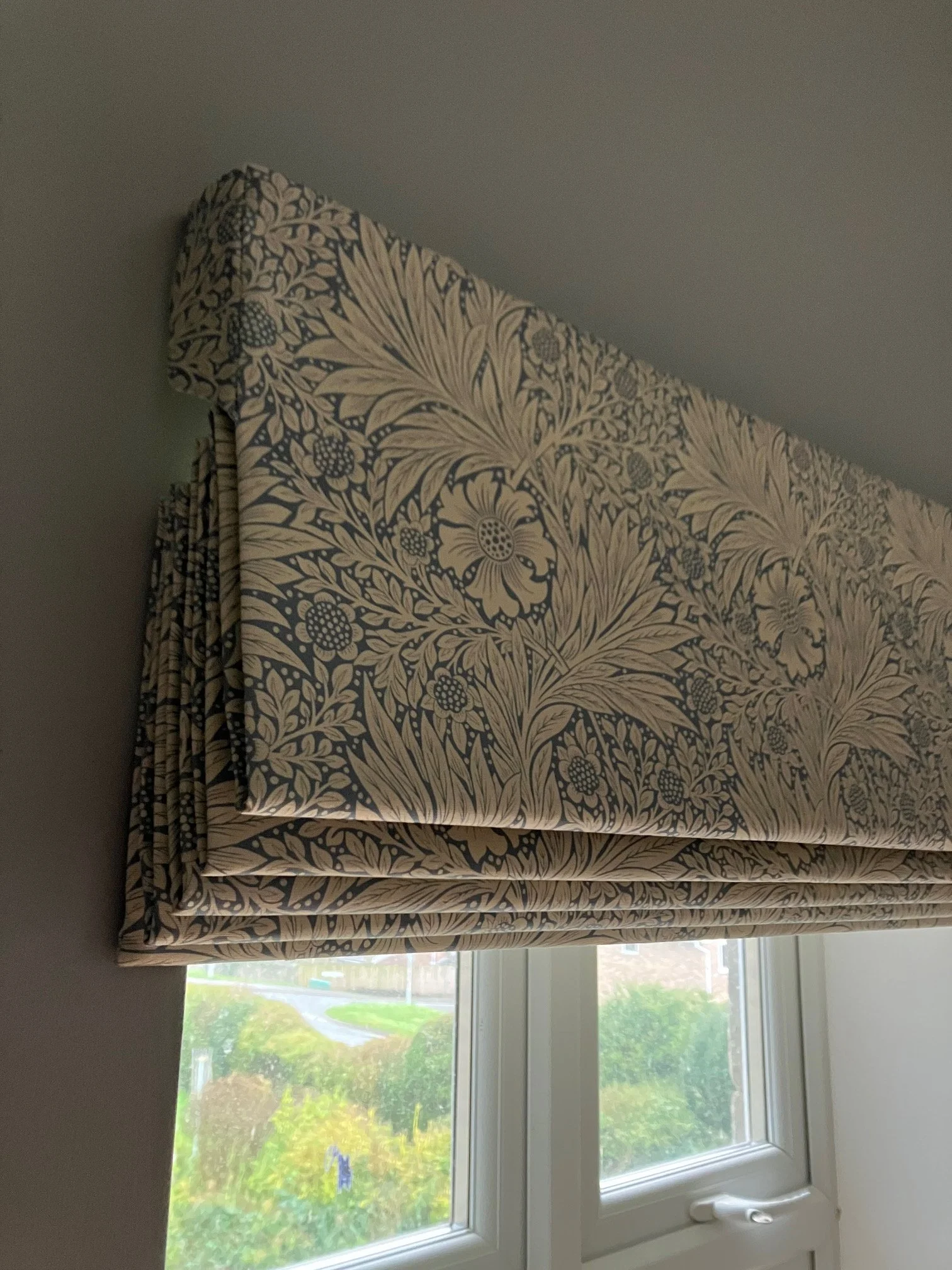 A William Morris Roman blind, looking out onto a green outdoor scene with trees and a small stream.