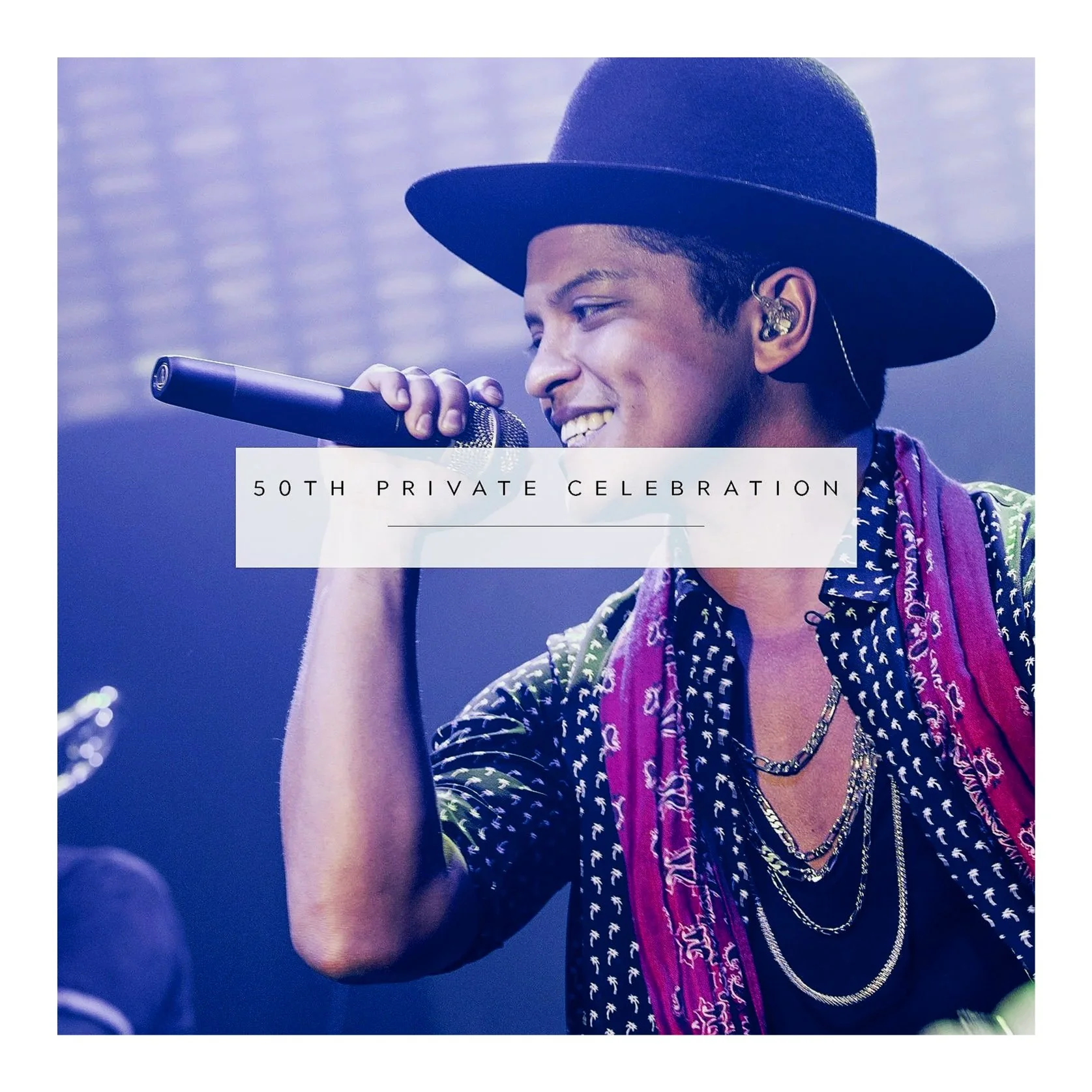 A young male singer wearing a black hat, patterned shirt, and layered necklaces while singing into a microphone at a private celebration event.