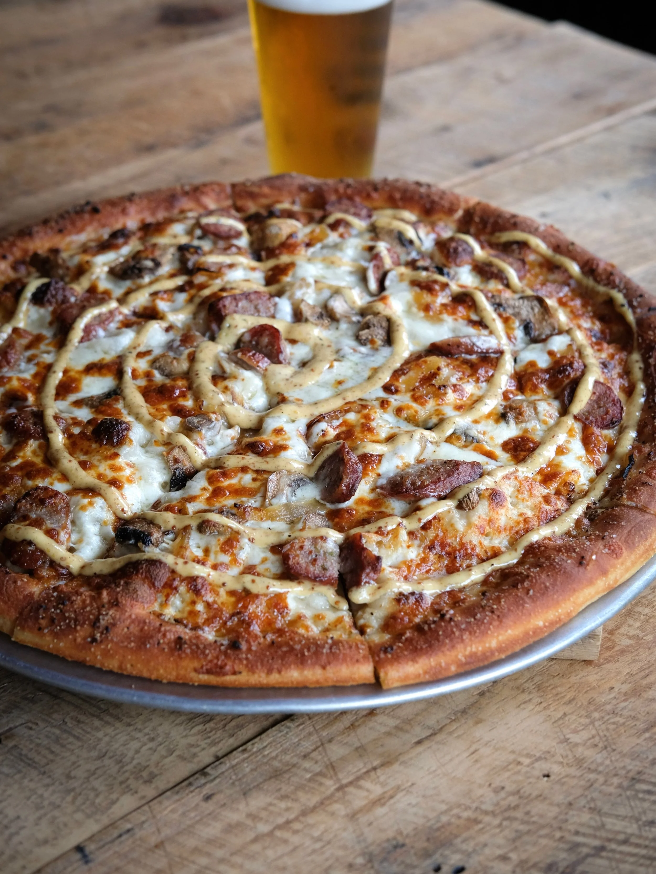 BEER-BRAISED SAUSAGE PIZZA
A Fall Tradition. Blue cheese base topped with beer-braised sausage, caramelized onion, and mushroom.
Finished with a brewpub mustard swirl and Montreal-seasoned crust.
