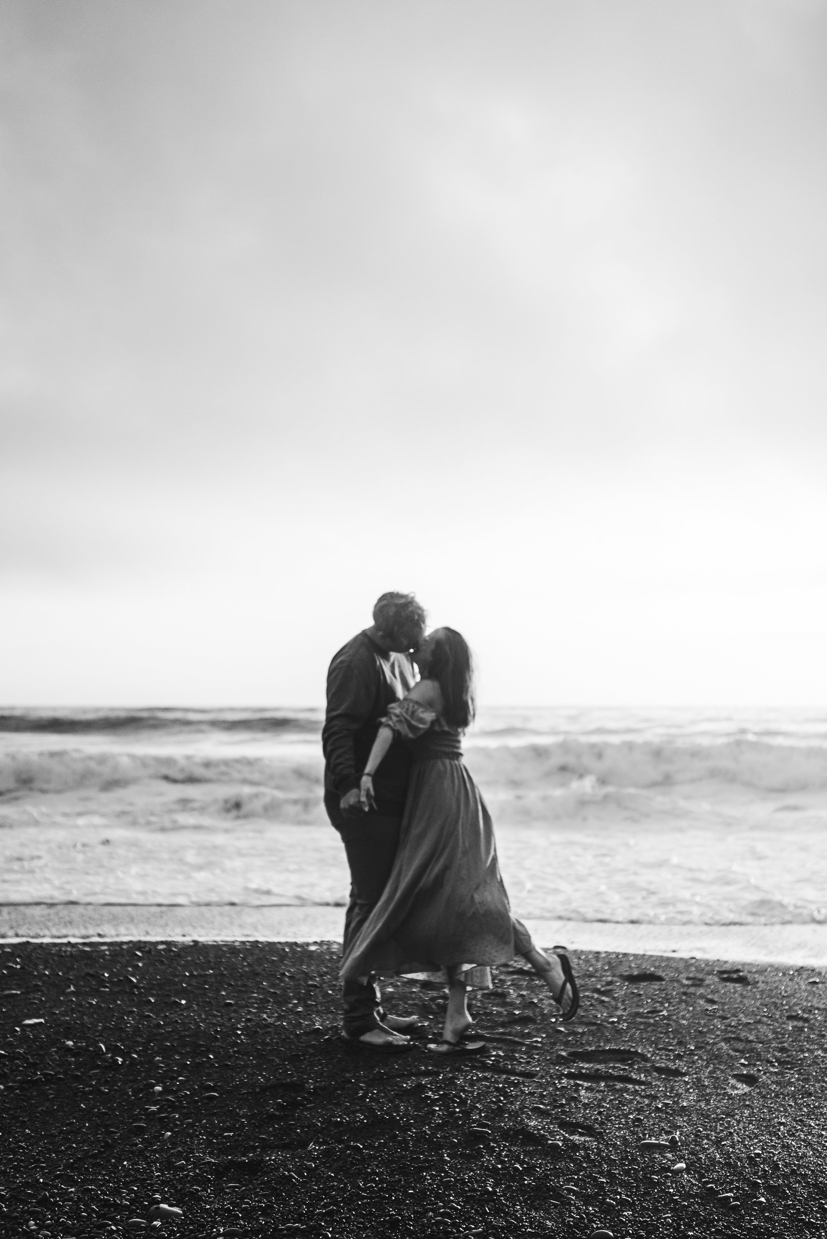 man and woman kissing on the beach with ocean in the background