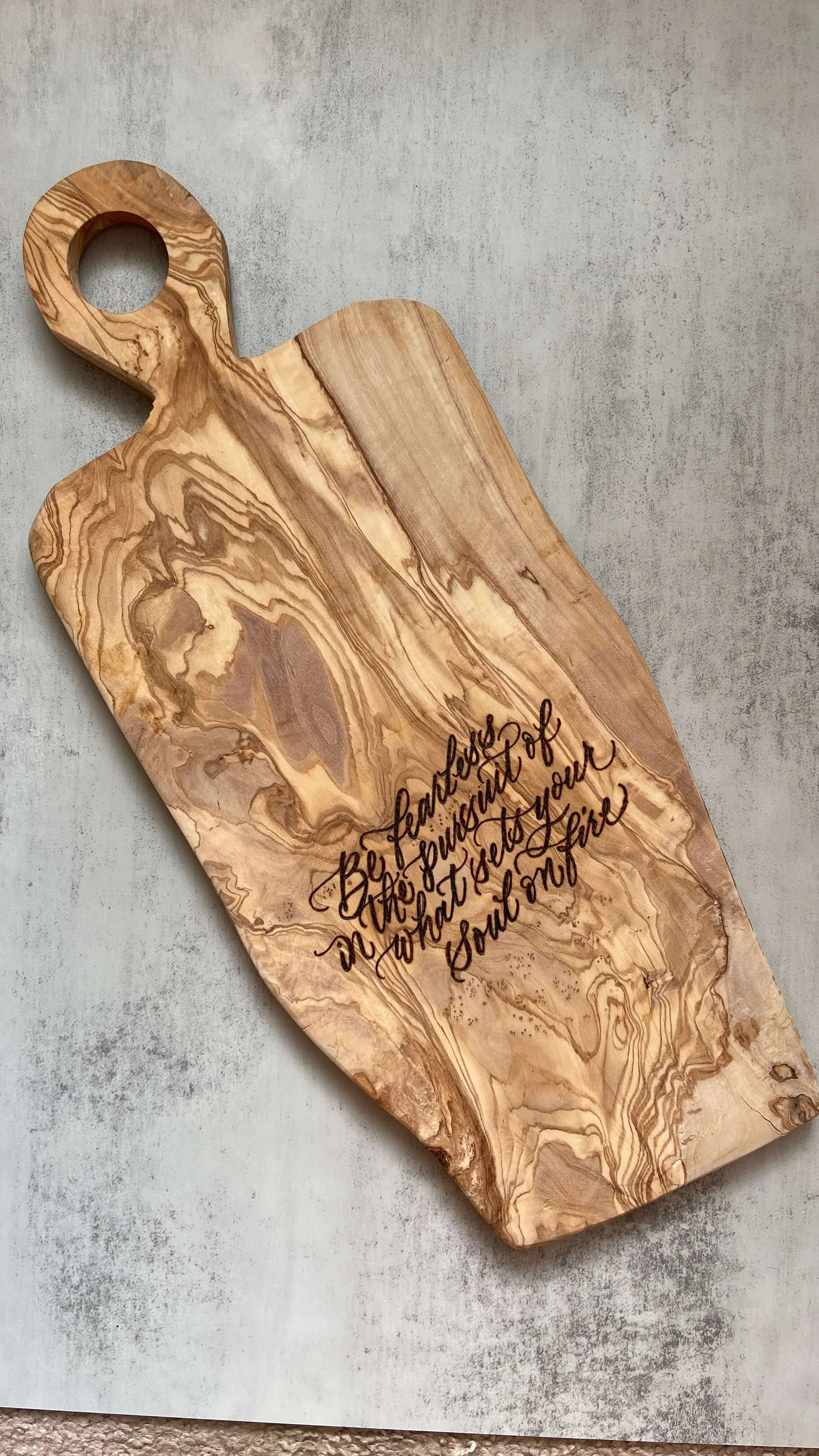 an olivewood cheeseboard with a quote wood-burned onto it