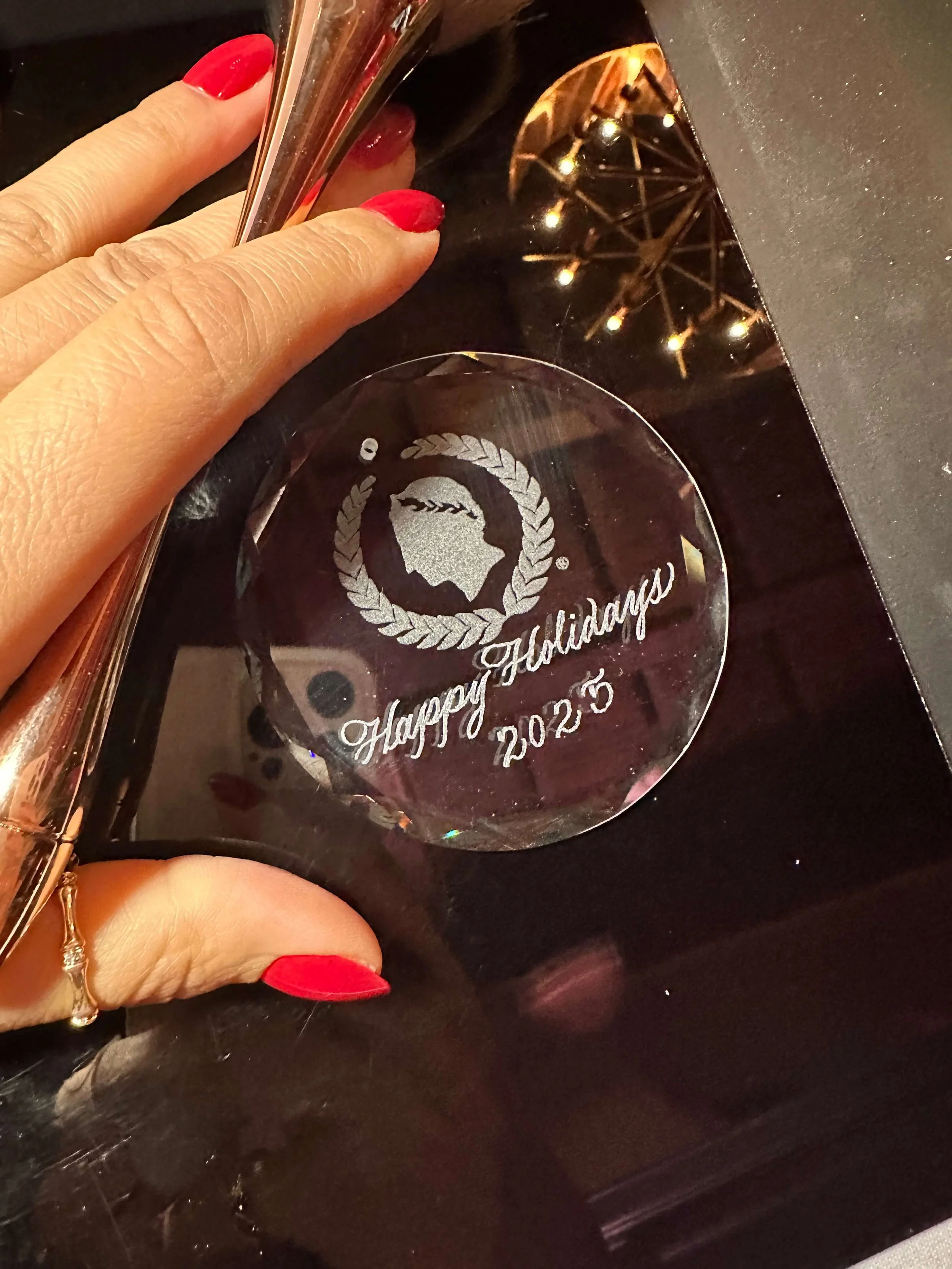 "Happy Holidays 2025" engraved onto a glass ornament  with the Caesar's logo on it. 