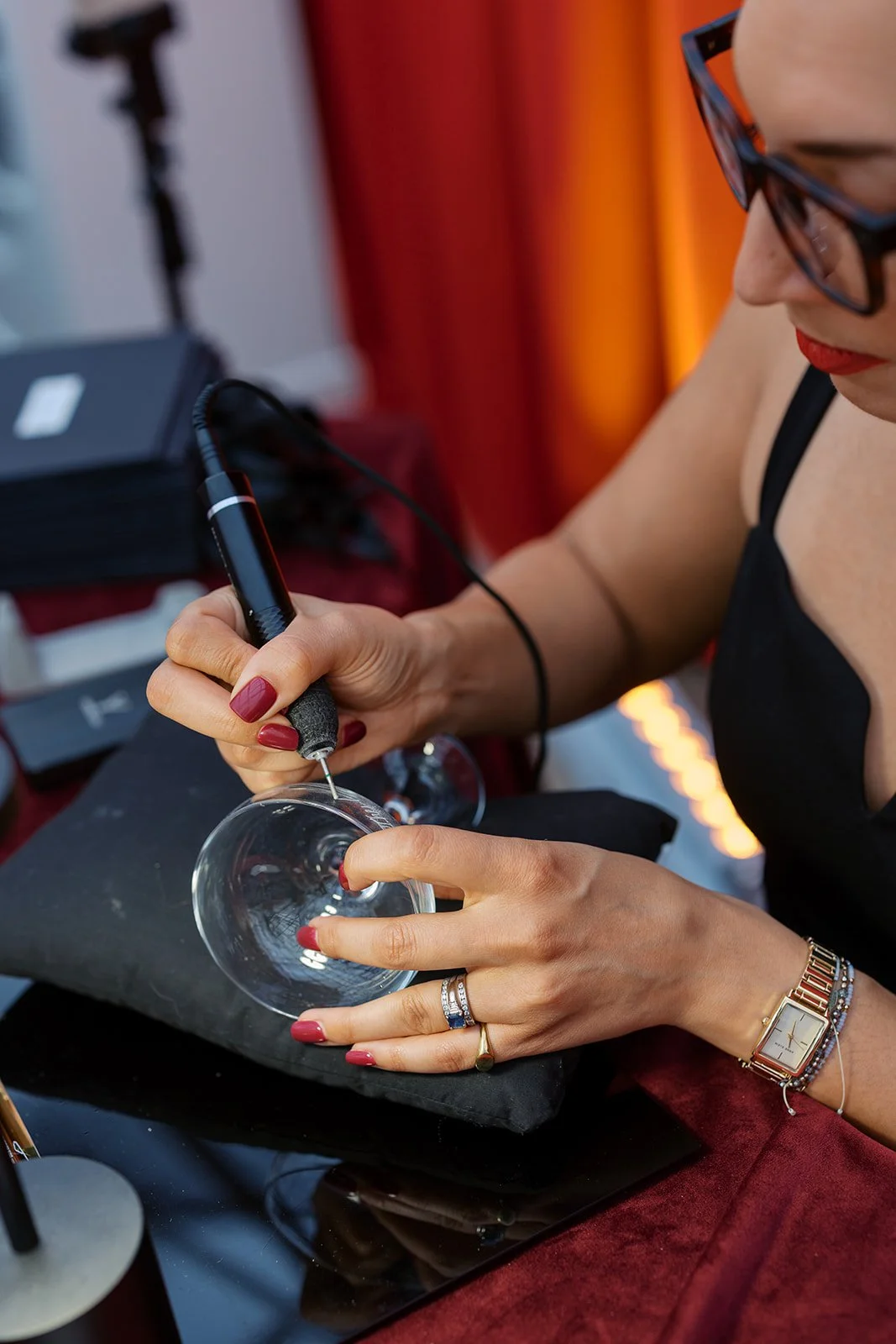 A woman's hand with red nails holding a black hand engraving drill and a copper kentucky derby cup