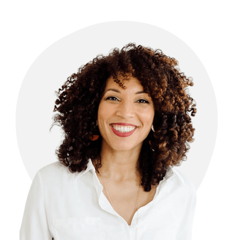 Smiling woman with curly brown hair wearing a white blouse against a white background.