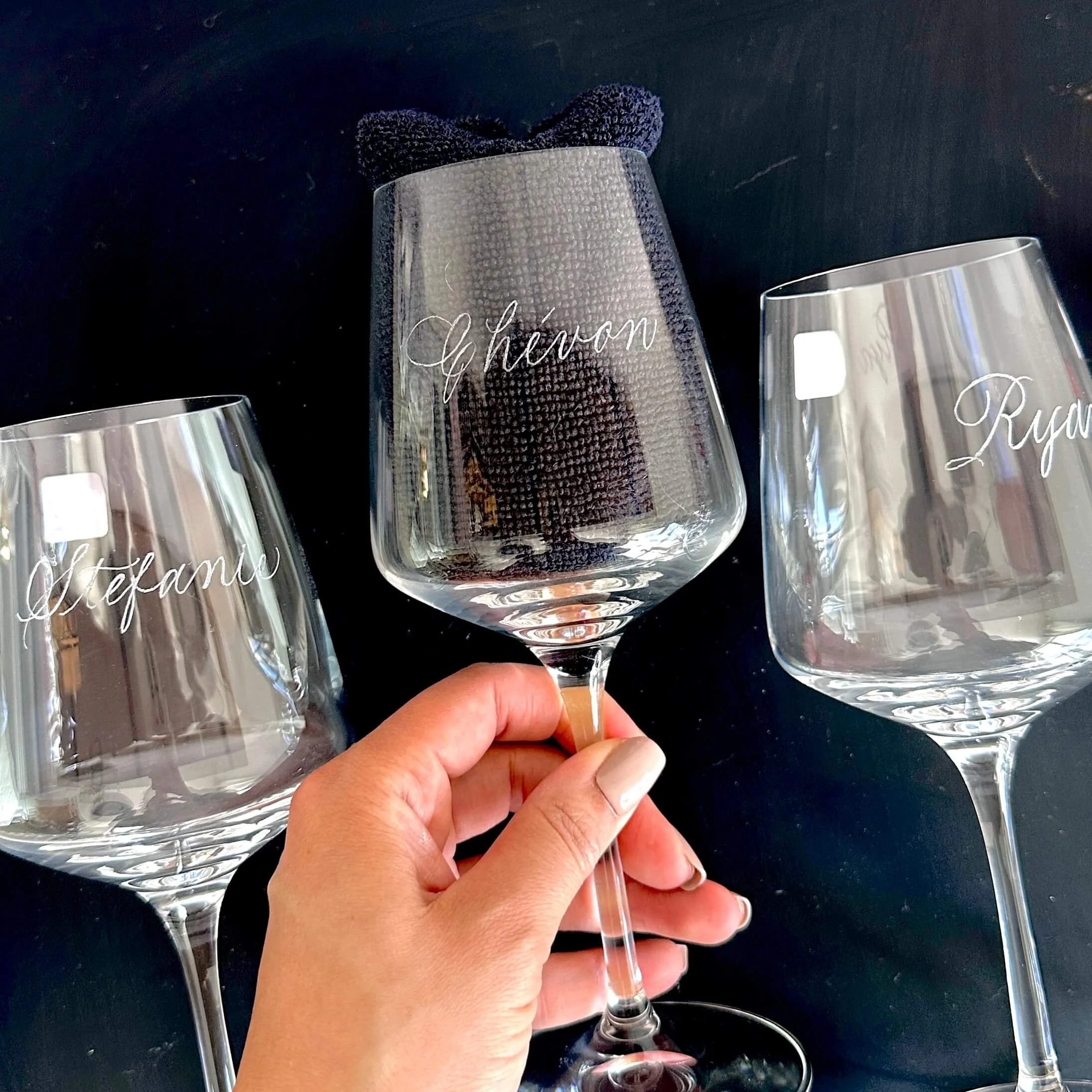 Woman's hand holding a wine glass with the name "Chevon" engraved on the front