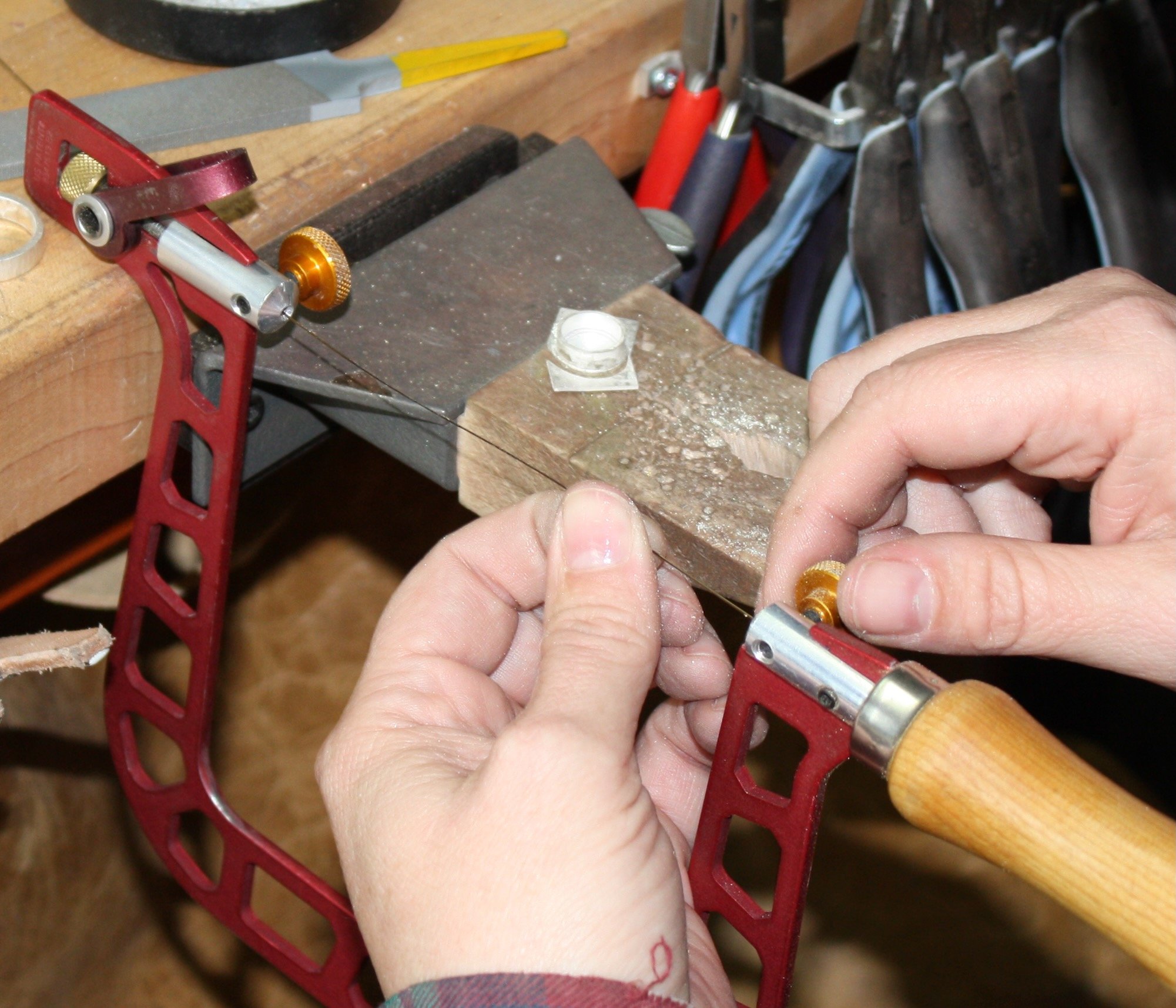Hand holding a piece of wood while using a cutting tool in a woodworking workshop, with tools and materials in the background.