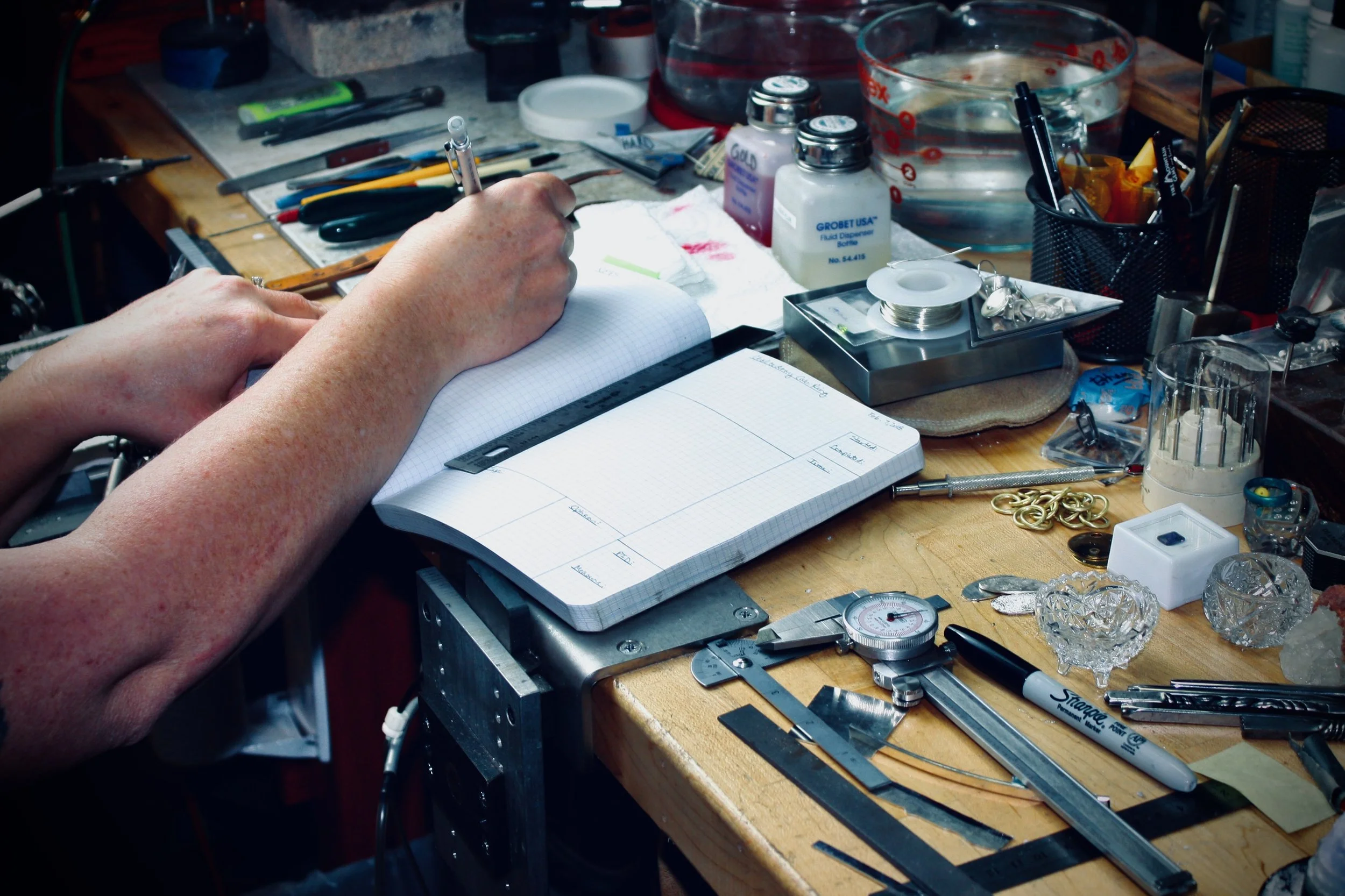 jewelers hands recording measurements at jewelers workbench with jewelry tools