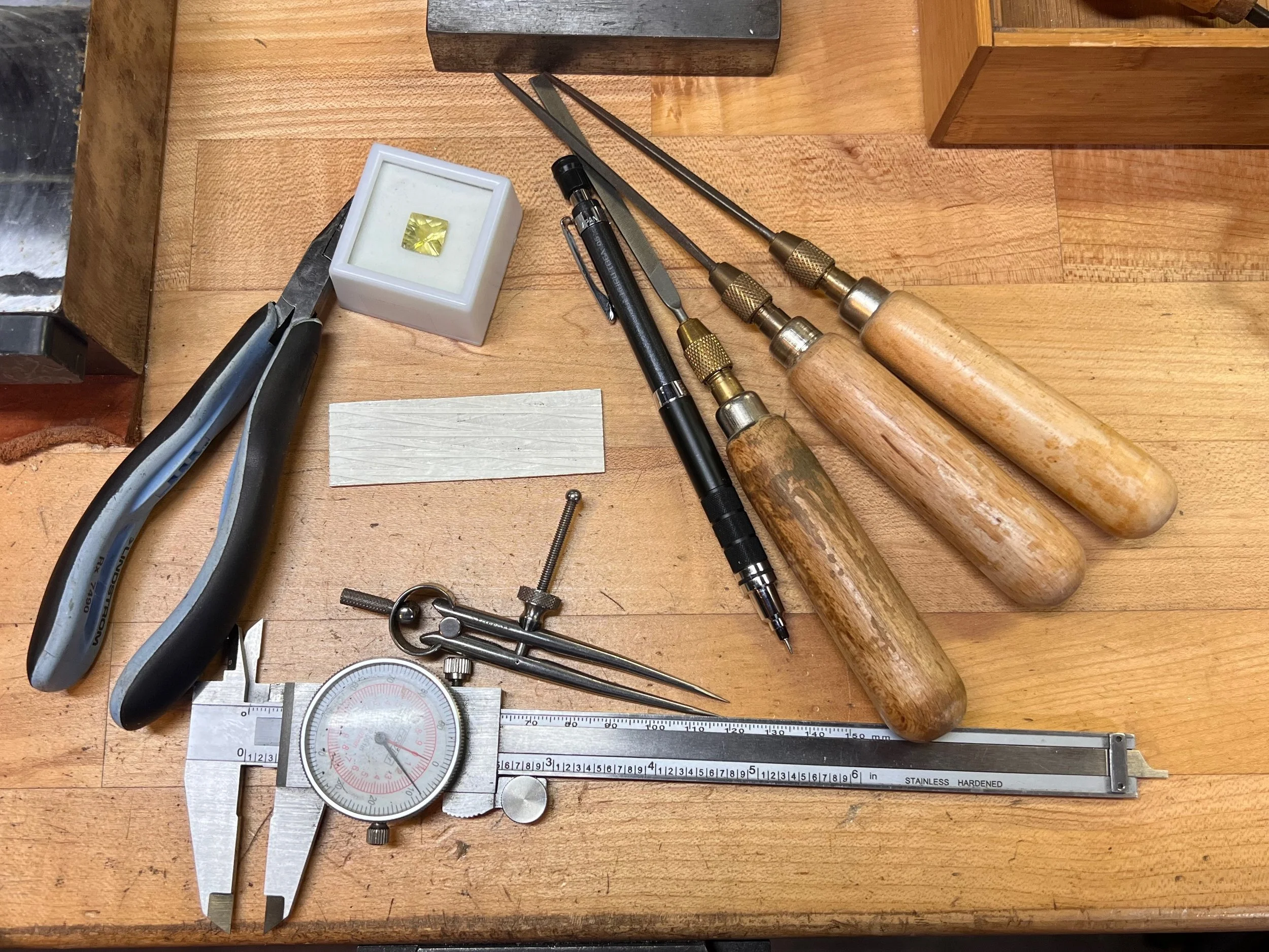 Jewelry Tools on a workbench calipers files pencil square faceted stone pliers