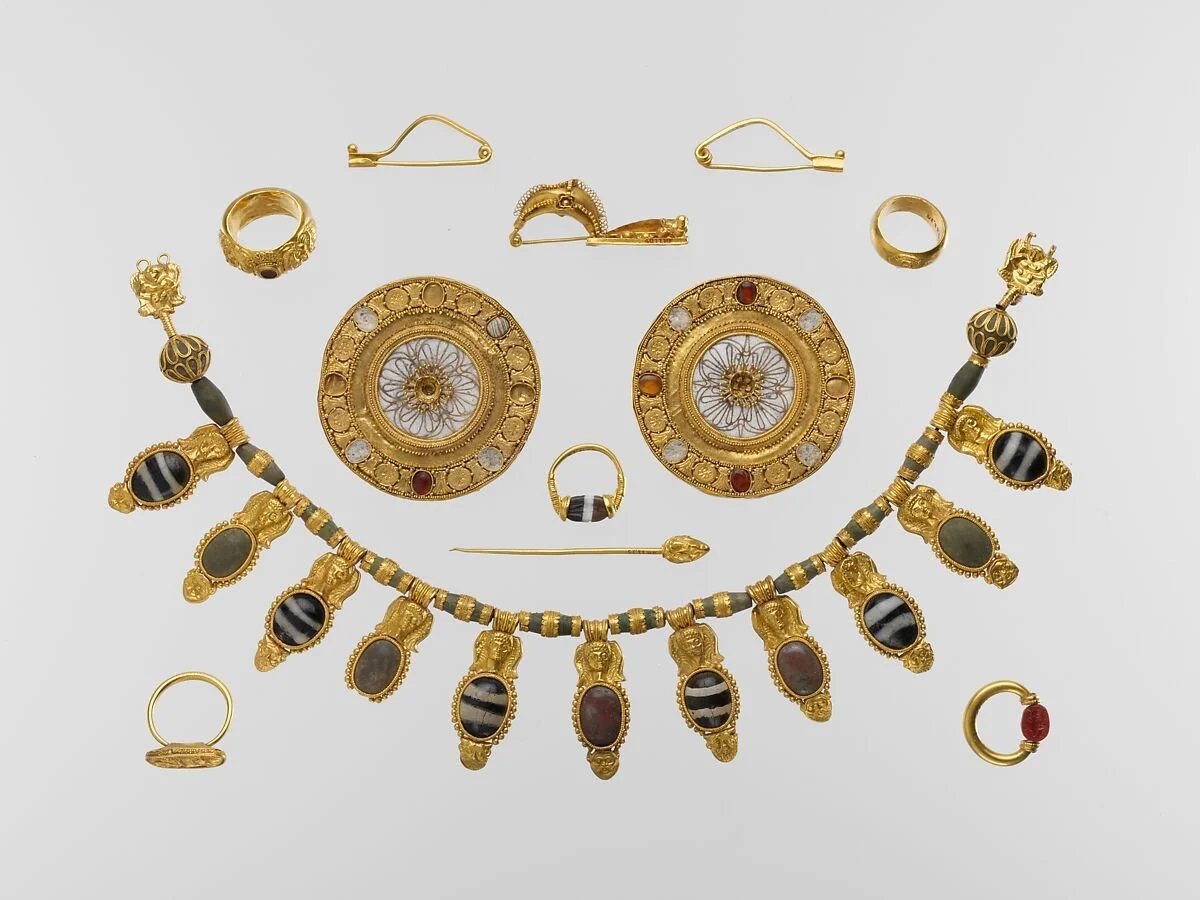 Etruscan jewelry set with gold necklaces, rings, fibulae, earrings, and gemstones, showing ancient granulation, repetition, and geometric design.