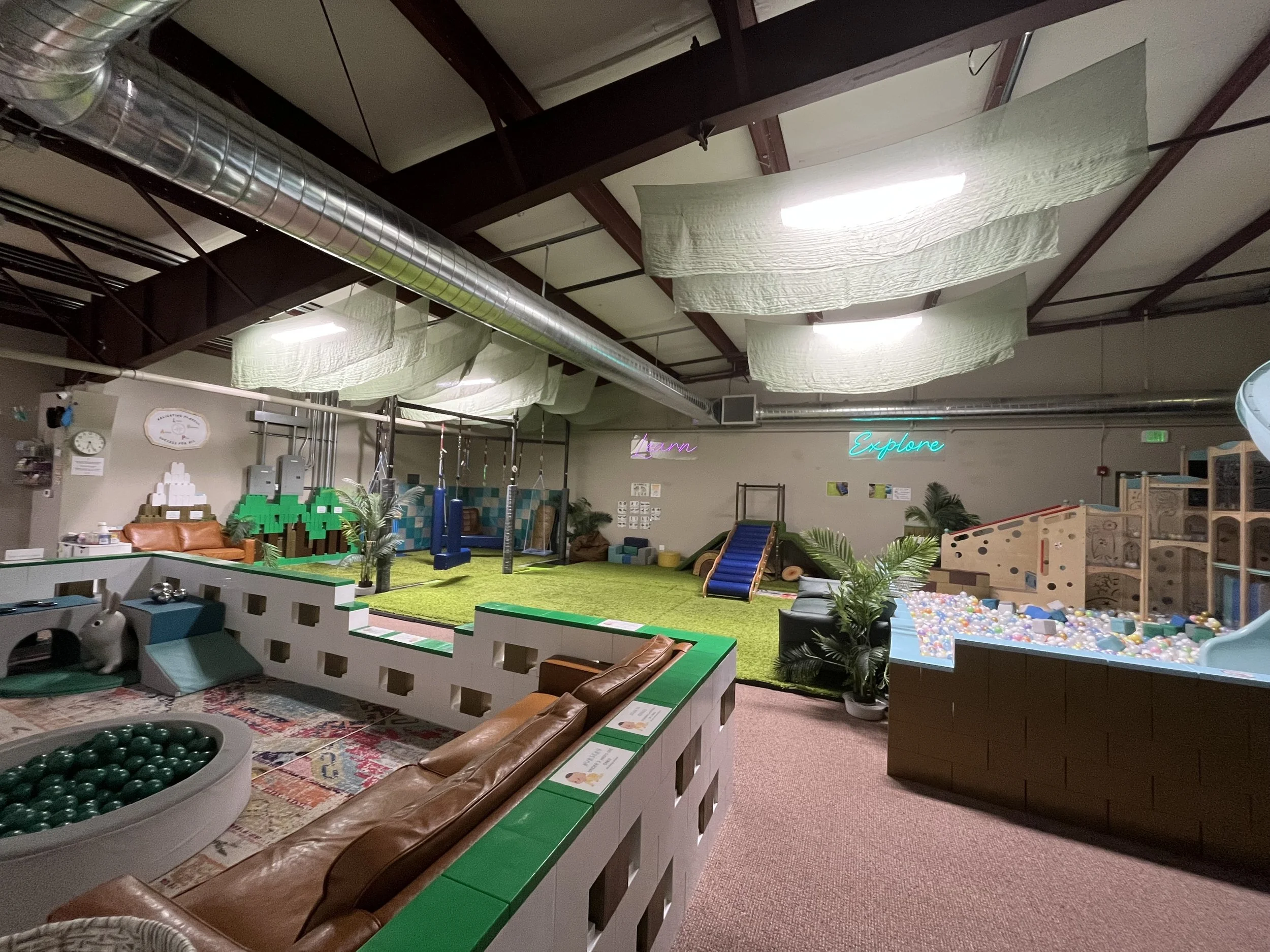 Indoor play area with swings, slide, ball pit, seating, and decorative plants.