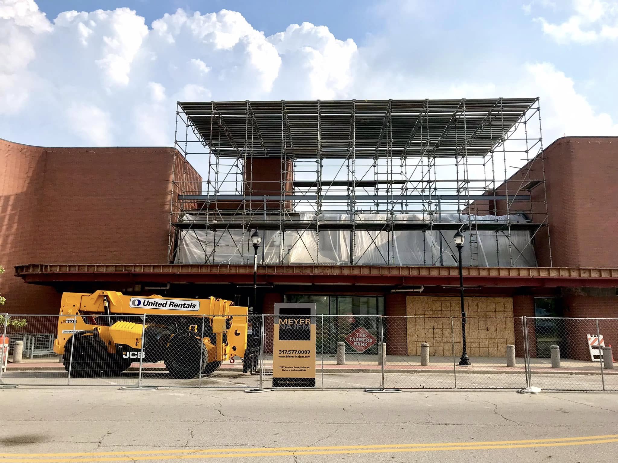 Construction scaffolding set up in front of a red brick building under a partly cloudy sky.