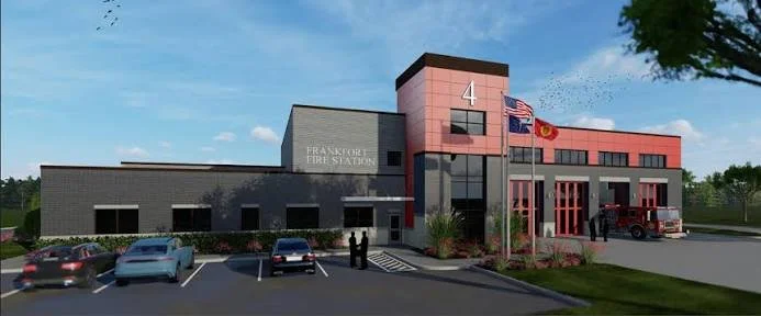 Frankfort Fire Station building with a parking lot and flags in front, under a partly cloudy sky.