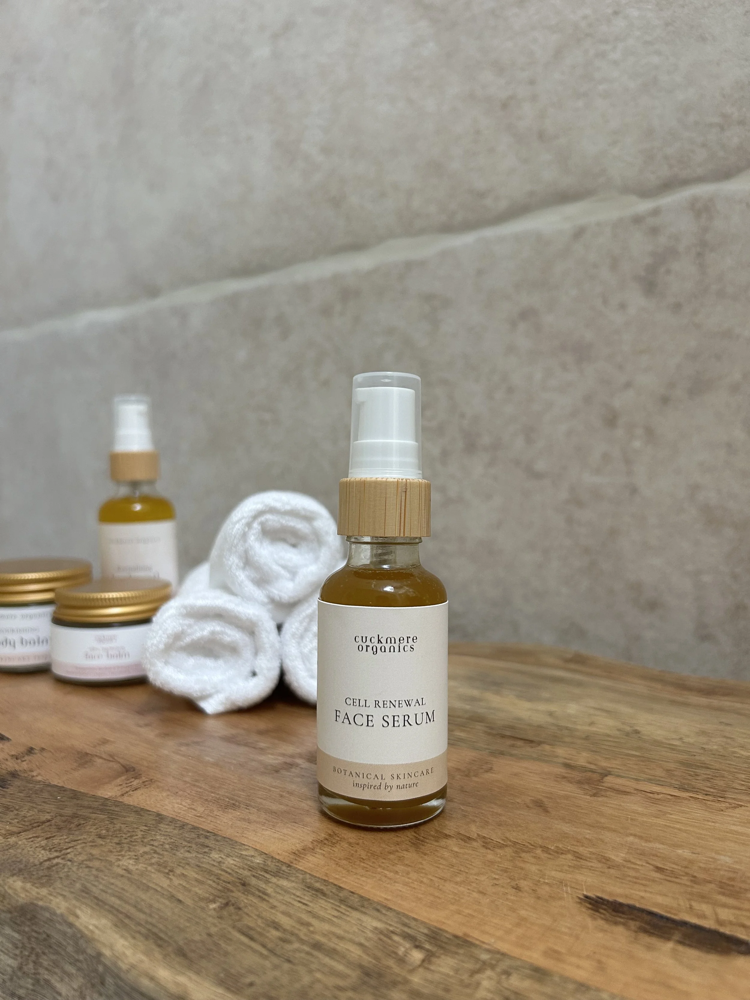 Cuckmere Organics Cell Renewal Face Serum in a glass bottle, on a wooden surface with rolled white towels behind.