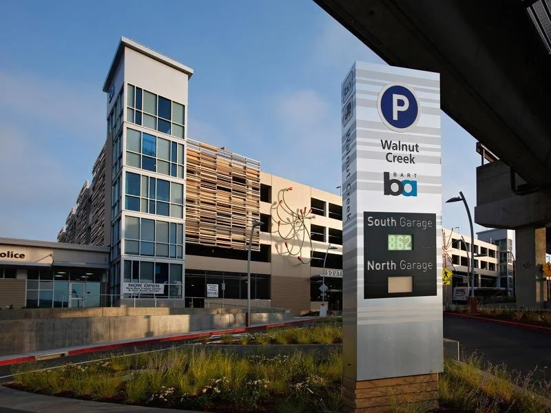 Parking garage at Walnut Creek BART station with signage for South Garage and North Garage, and a modern building in the background against a blue sky.