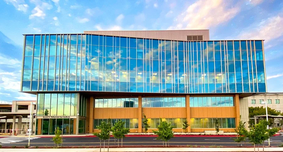 Modern multi-story office building with reflective glass windows on the upper floors and a tan facade on the lower floors situated in an urban area.