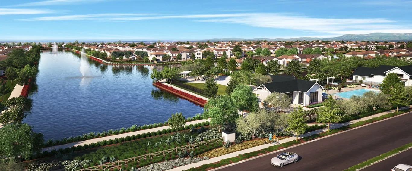 Aerial view of a residential community featuring a large pond with a fountain, surrounded by trees, pathways, and houses with swimming pools, under clear blue skies.