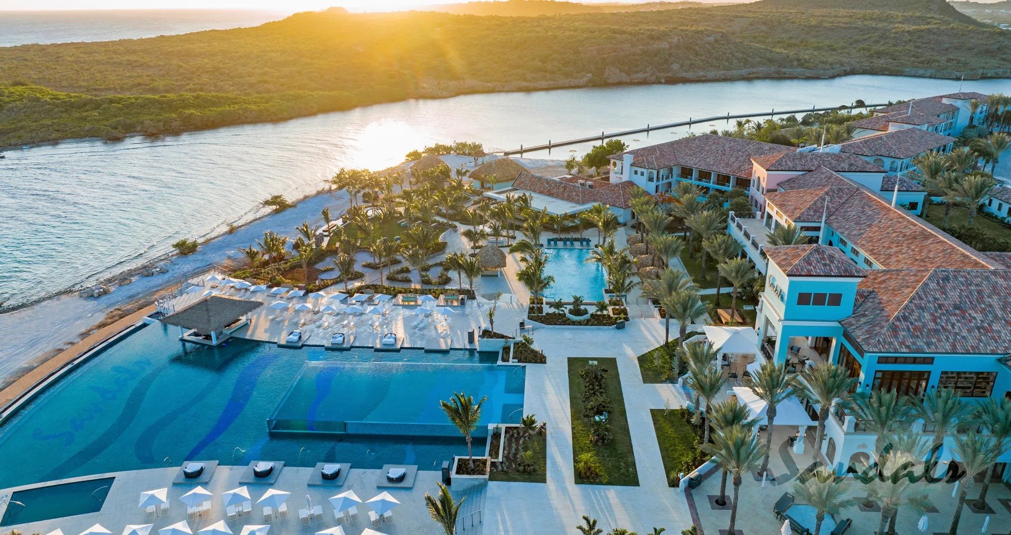A luxurious Curacao resort features an inviting pool surrounded by palm trees, offering breathtaking ocean views, epitomizing the ultimate island vacation experience.