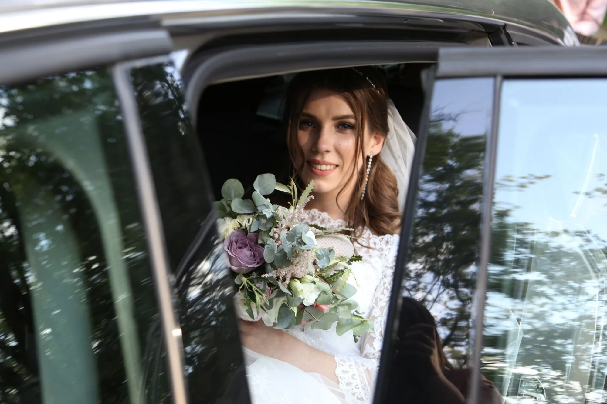 Bride smiling from car window with bouquet on the way to ceremony—on-time wedding day transportation