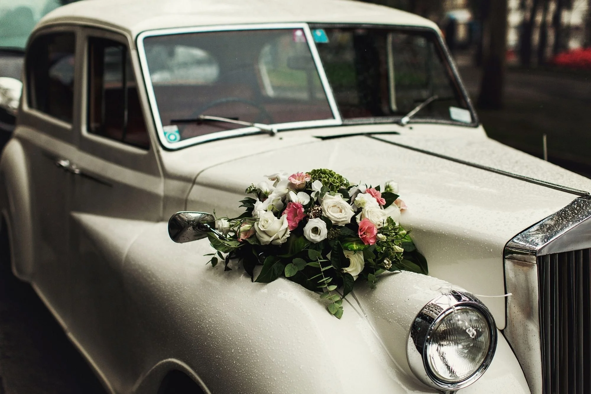 Vintage white wedding car with floral arrangement on hood—stylish couple getaway vehicle